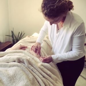 woman lying on a treatment bed, draped with towels receiving acupuncture from an acupuncturist