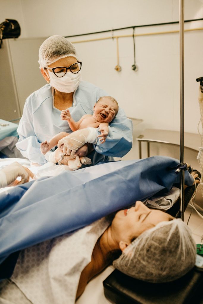 Repairing the uterus after C-section doctor holding baby after c-section with mother lying on the table