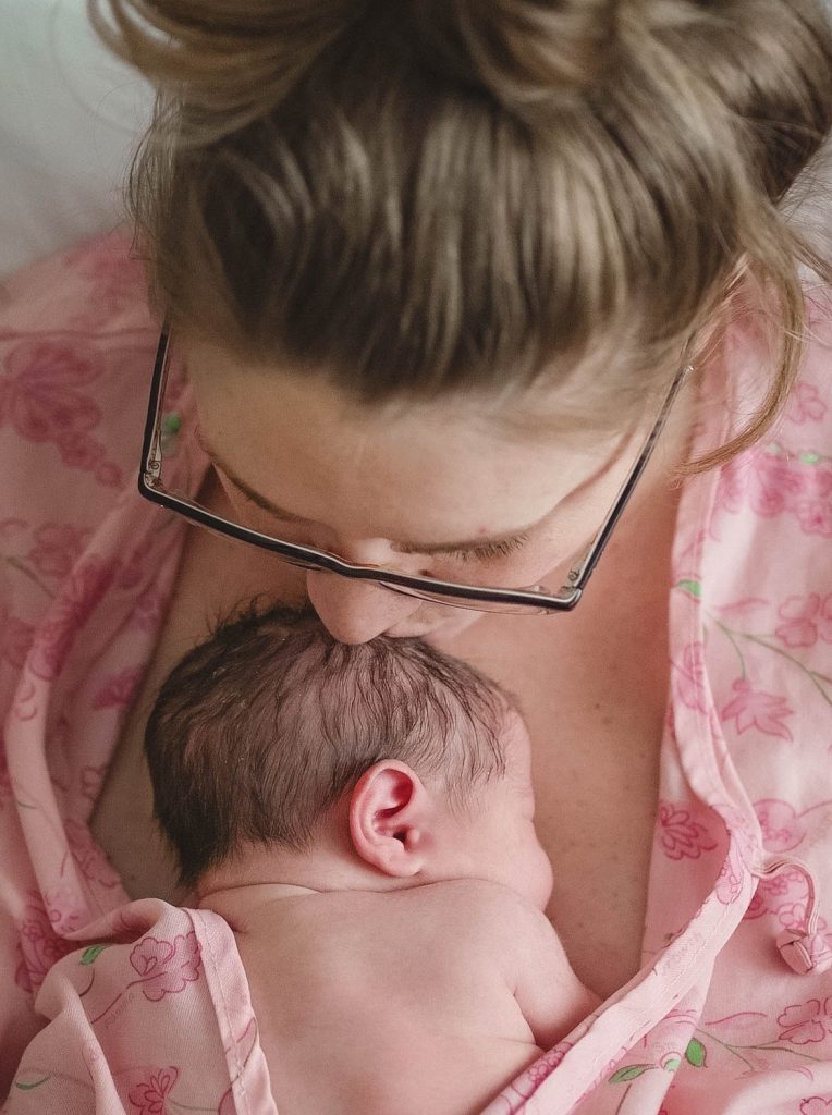 postpartum mother kissing newborn baby